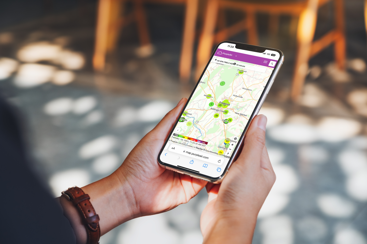 Hand holding a mobile device showing the Purple Air Monitoring App