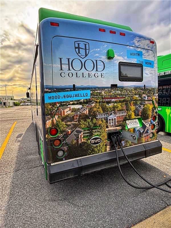 This image shows the rear of a BYD bus that is charging at a charging station, covered by a graphic