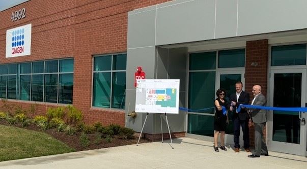 3 people cut a ribbon in front of a brick building