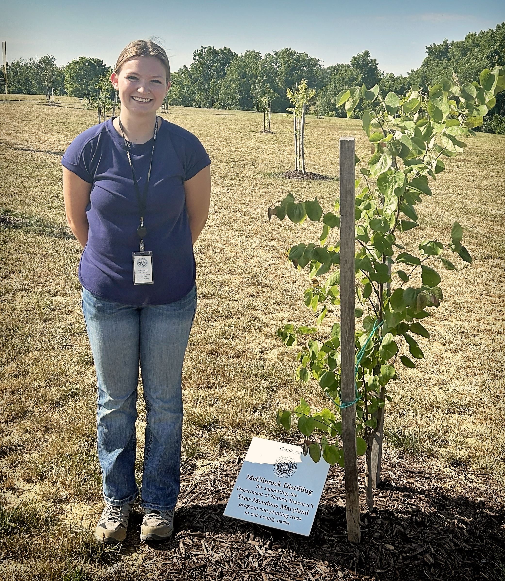 Photo of Abbie Peterson next to a newly planted tree